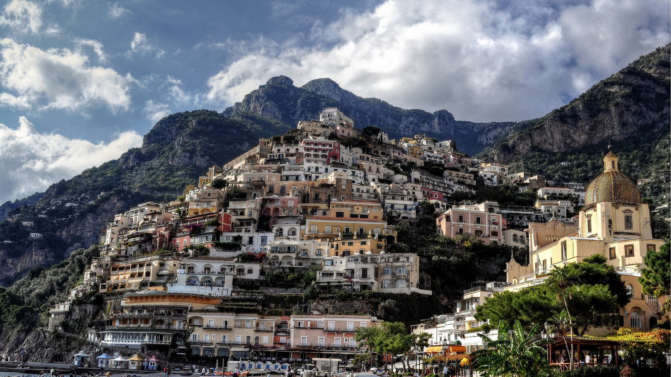 White and Brown Concrete Buildings Near Mountain Under White Clouds During Daytime. Wallpaper in 2560x1440 Resolution