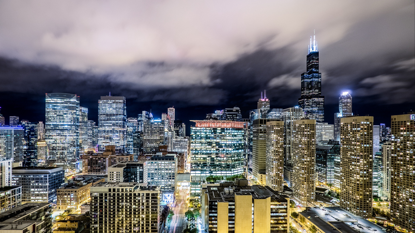 City With High Rise Buildings Under Gray Clouds During Night Time. Wallpaper in 1366x768 Resolution