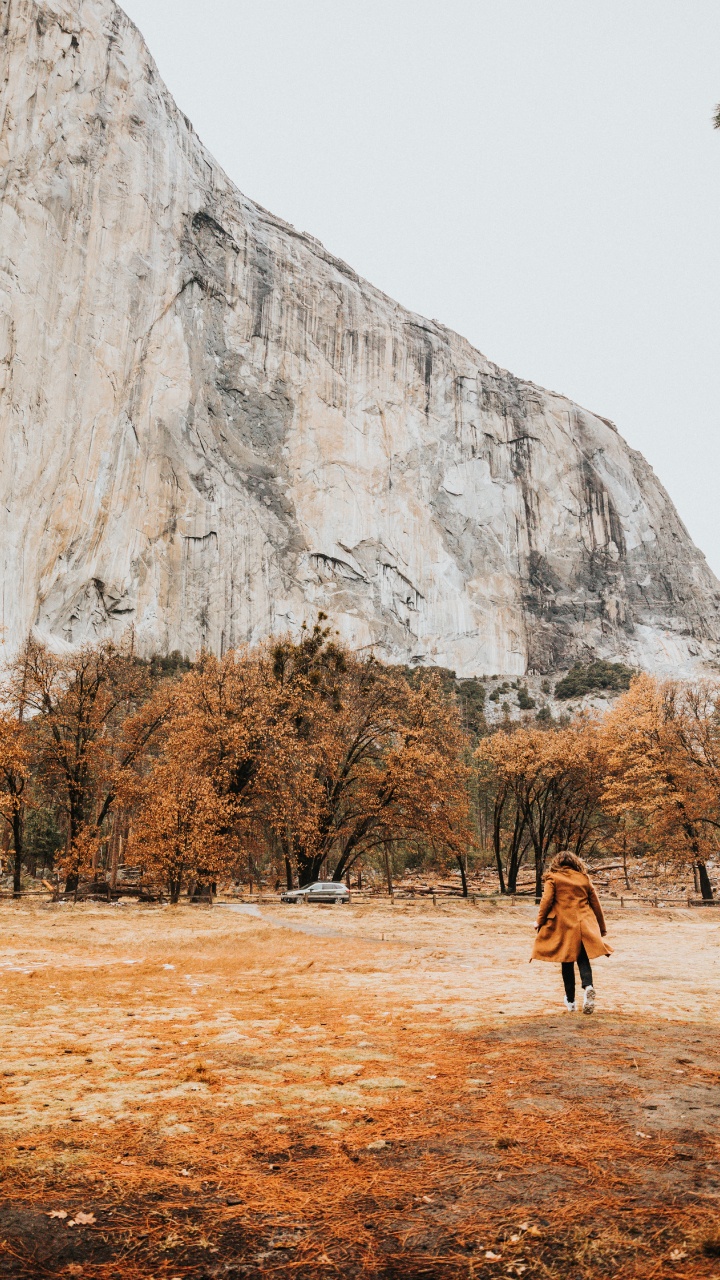 Person in Brown Coat Walking on Brown Field Near Gray Rock Mountain During Daytime. Wallpaper in 720x1280 Resolution