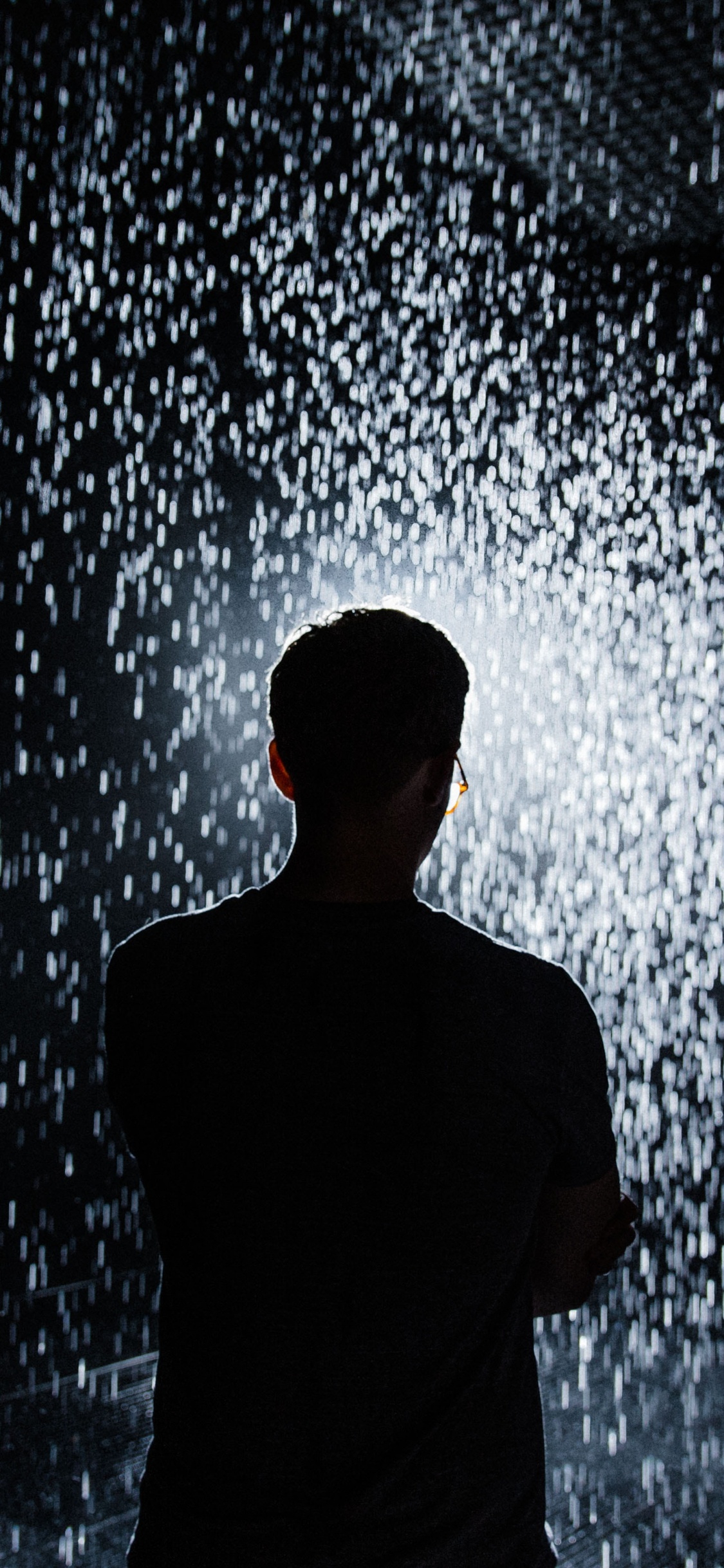 Man in Black Shirt Standing in Front of Water Splash. Wallpaper in 1125x2436 Resolution