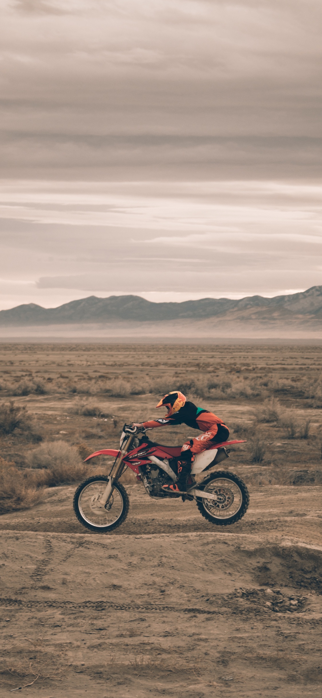 Hombre de Chaqueta Roja en Motocicleta Roja en Campo Marrón Durante el Día. Wallpaper in 1125x2436 Resolution