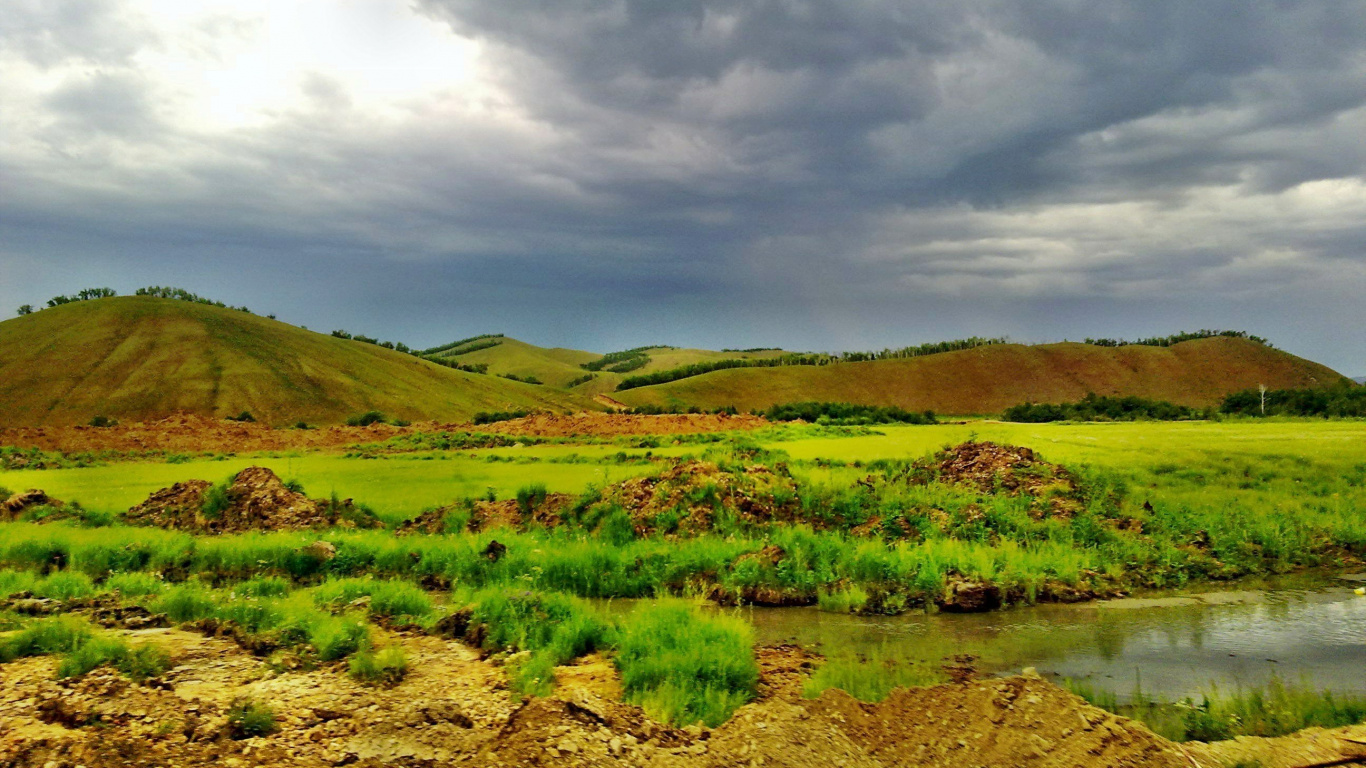 Campo de Hierba Verde Cerca Del Cuerpo de Agua Bajo un Cielo Nublado Durante el Día. Wallpaper in 1366x768 Resolution