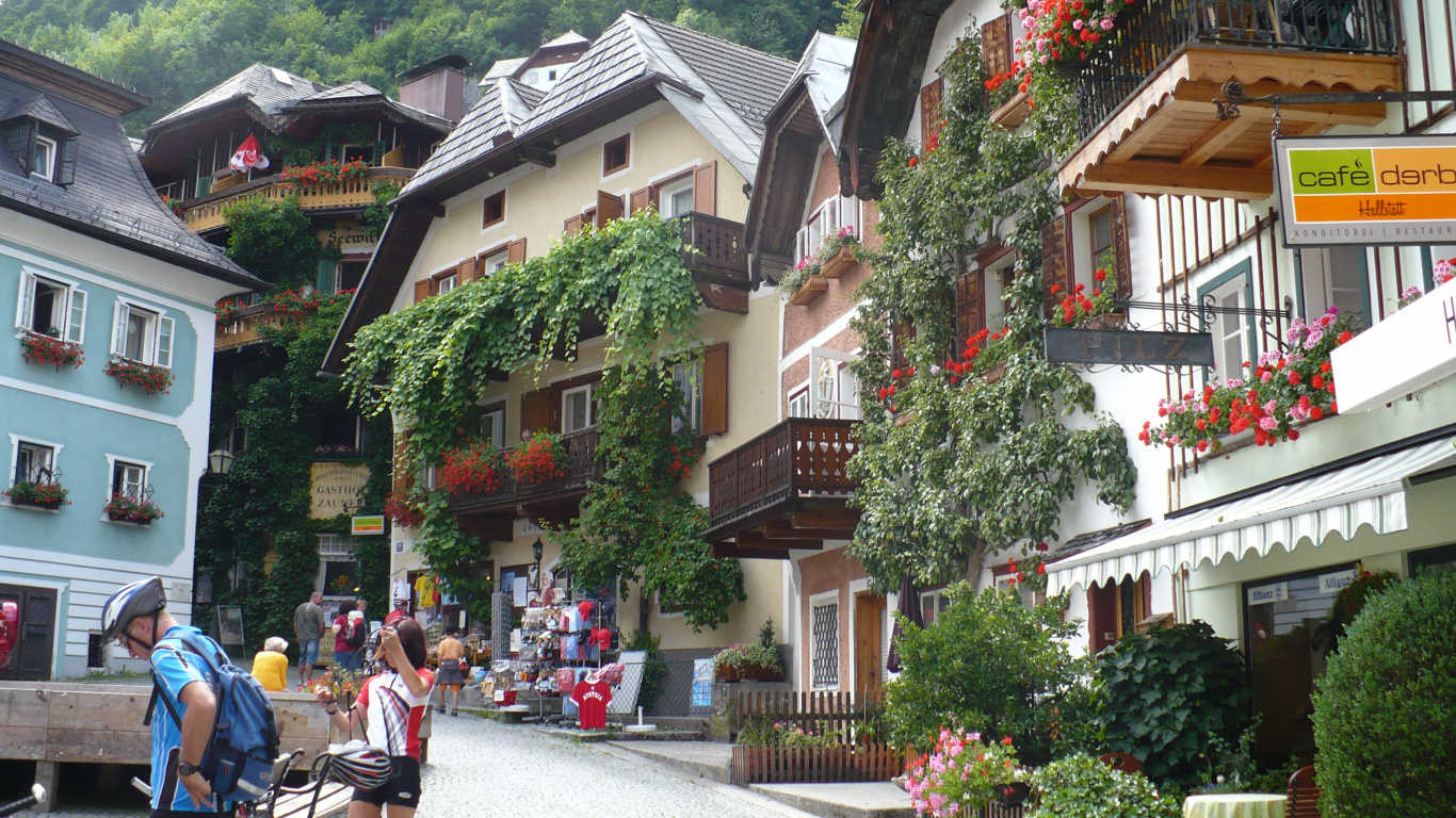 Personas Sentadas en un Banco Cerca Del Edificio de Hormigón Marrón y Blanco Durante el Día. Wallpaper in 1366x768 Resolution