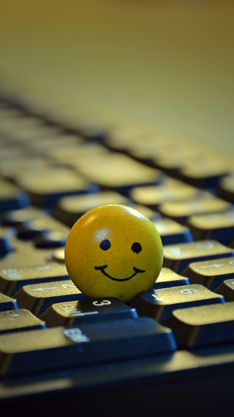 Gelber Smiley-Ball Auf Schwarzer Computertastatur. Wallpaper in 750x1334 Resolution