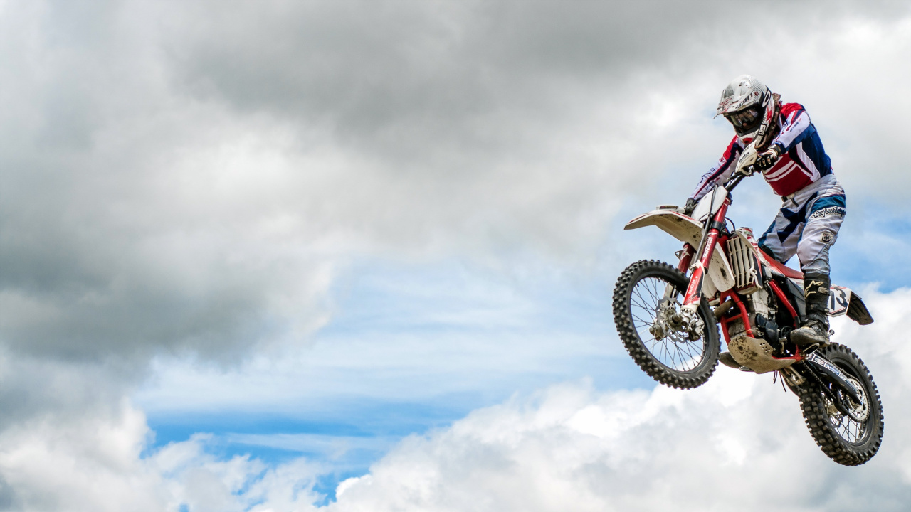 Hombre Montando Motocross Dirt Bike Haciendo Acrobacias Bajo Las Nubes Blancas Durante el Día. Wallpaper in 1280x720 Resolution