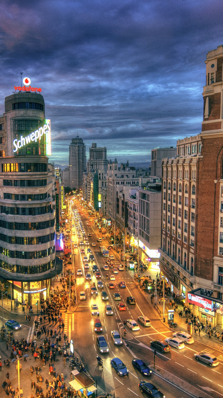 Autos Auf Der Straße Zwischen Hochhäusern Während Der Nacht. Wallpaper in 750x1334 Resolution