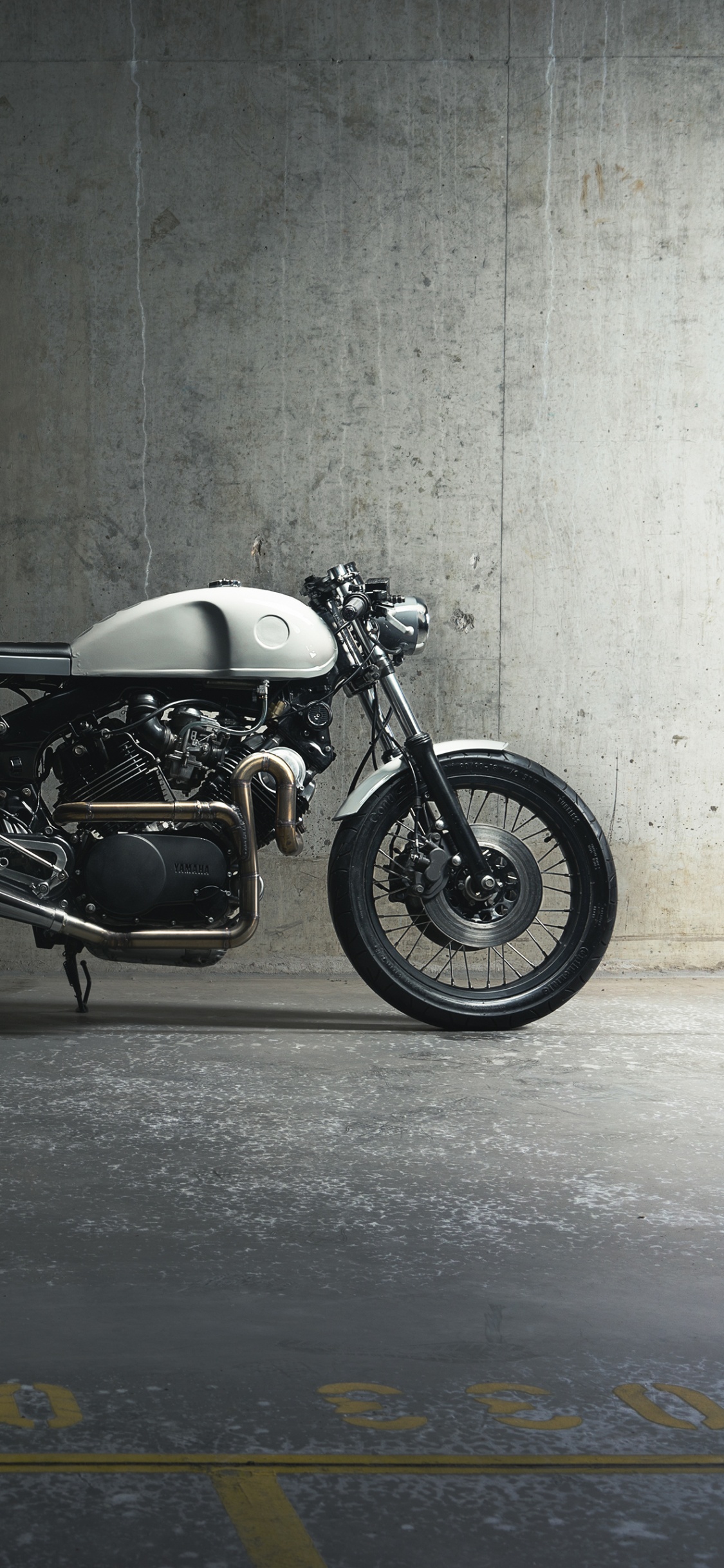 Schwarzes Und Silbernes Motorrad Neben Grauer Wand Geparkt. Wallpaper in 1125x2436 Resolution