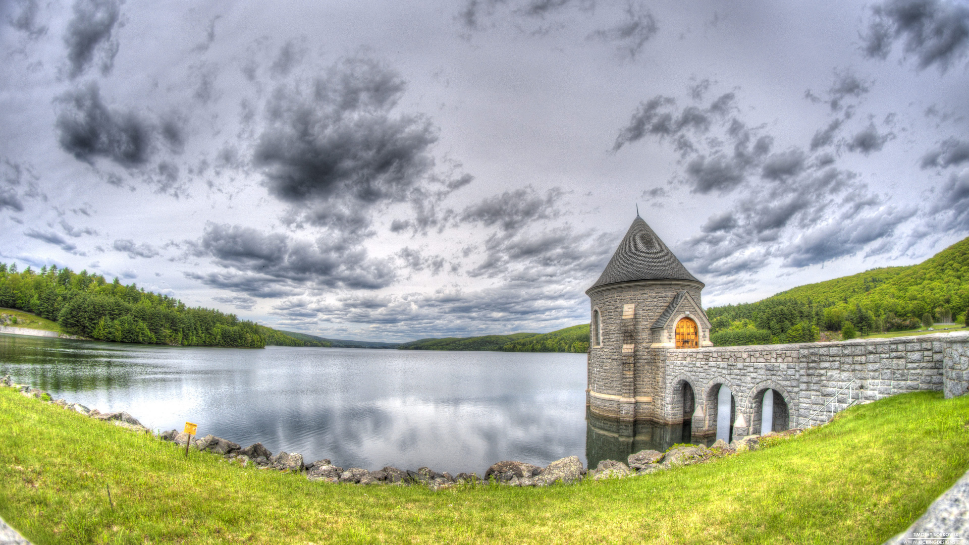 Gray Concrete Building Near Body of Water Under Gray Clouds. Wallpaper in 1920x1080 Resolution