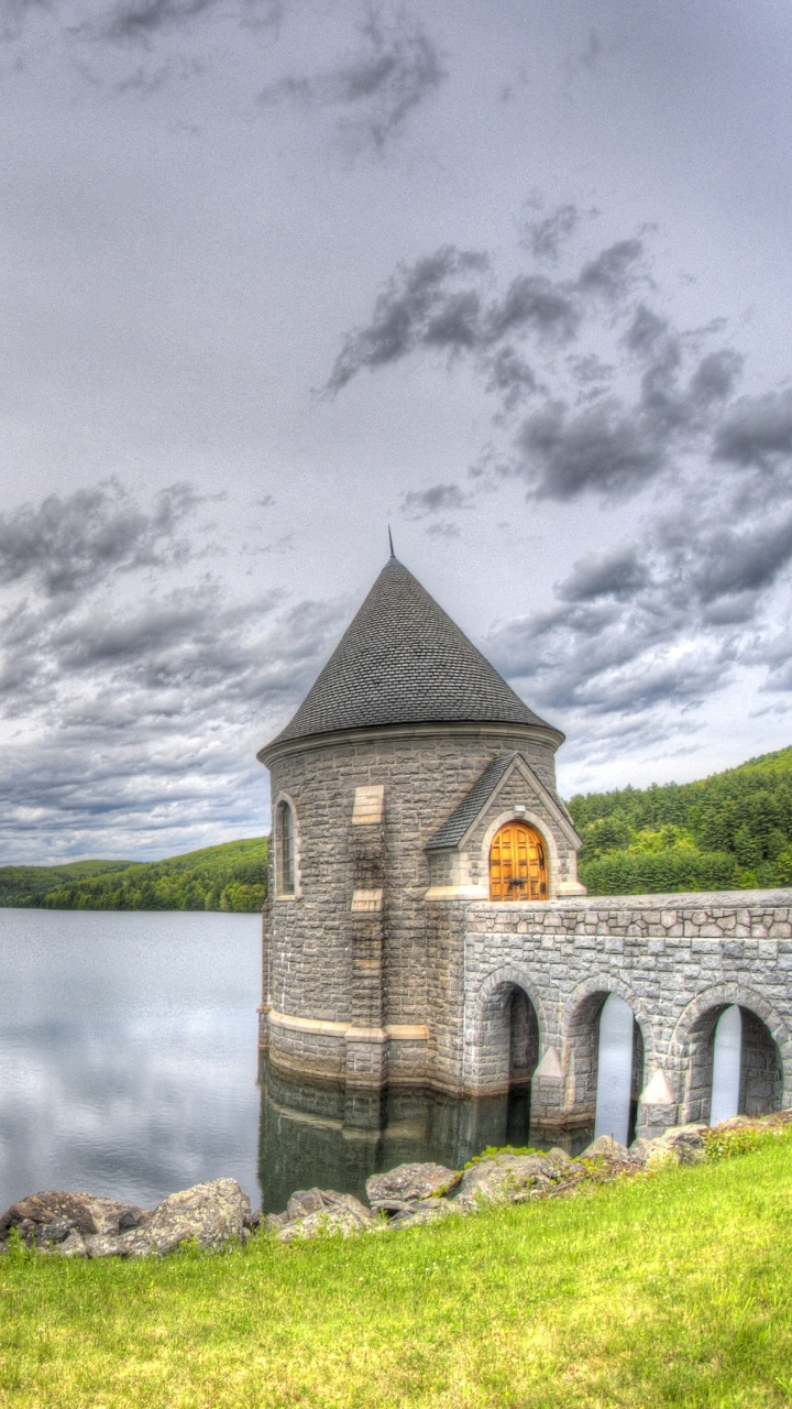 Gray Concrete Building Near Body of Water Under Gray Clouds. Wallpaper in 720x1280 Resolution