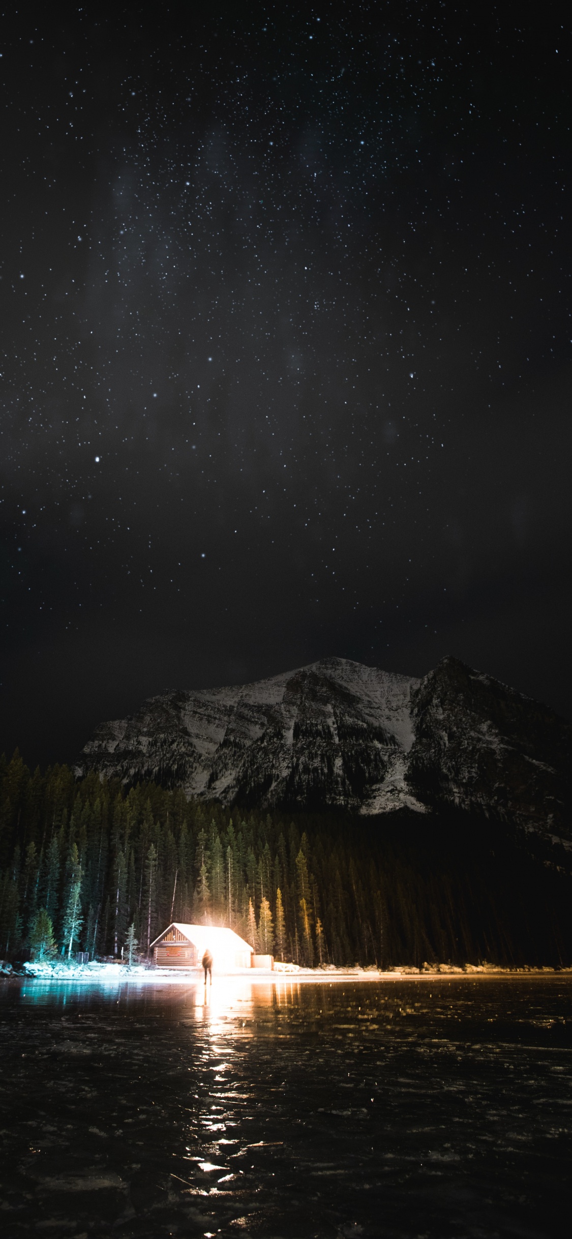 Person Standing on Water Near Mountain During Night Time. Wallpaper in 1125x2436 Resolution