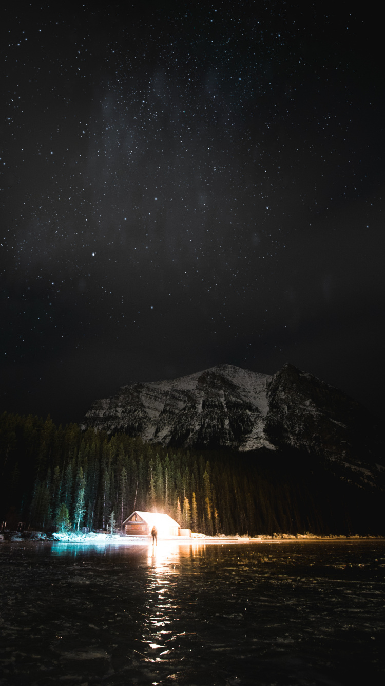 Person Standing on Water Near Mountain During Night Time. Wallpaper in 750x1334 Resolution