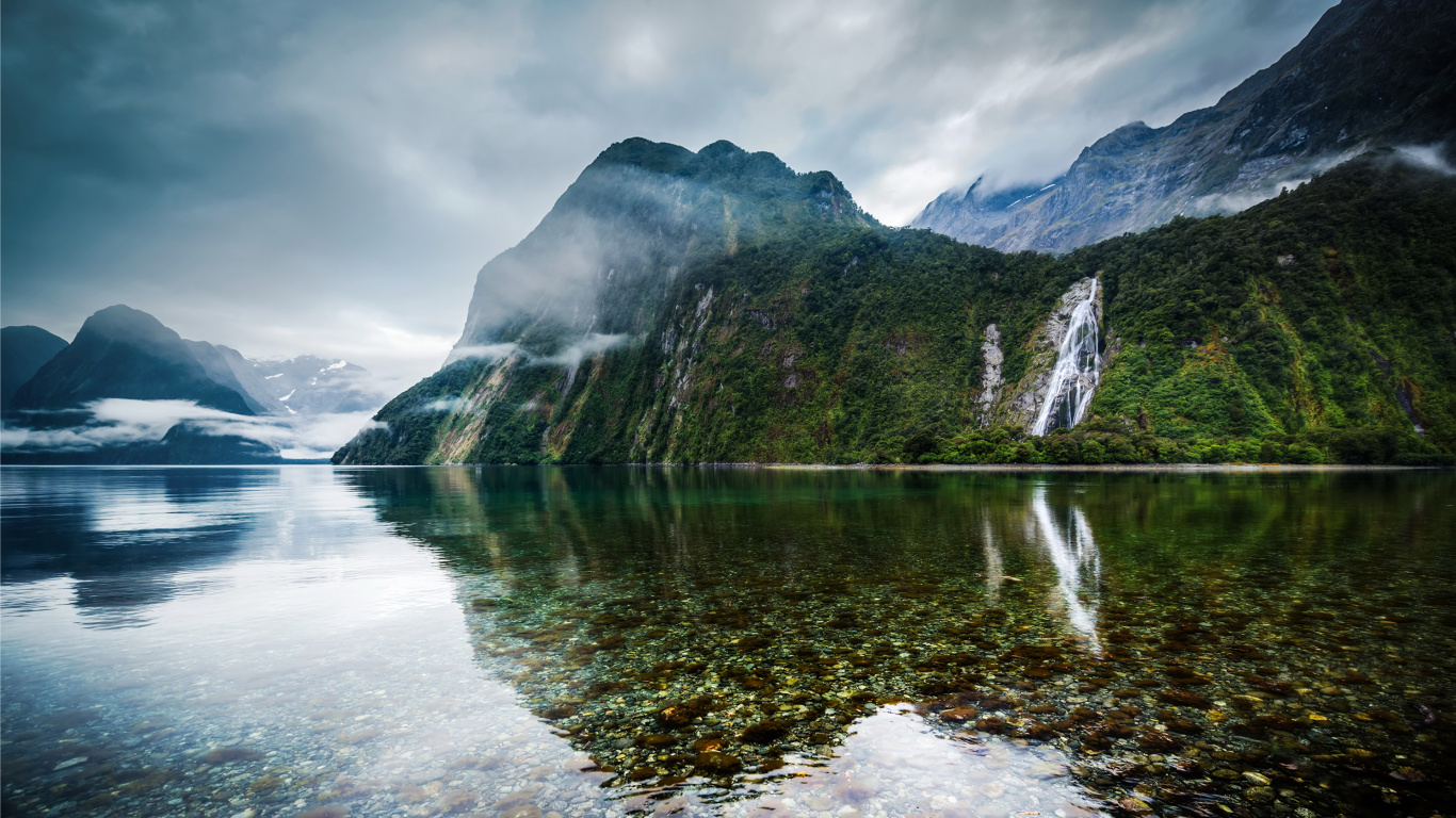Green and Brown Mountain Beside Body of Water Under Cloudy Sky During Daytime. Wallpaper in 1366x768 Resolution