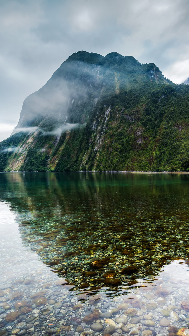 Green and Brown Mountain Beside Body of Water Under Cloudy Sky During Daytime. Wallpaper in 750x1334 Resolution