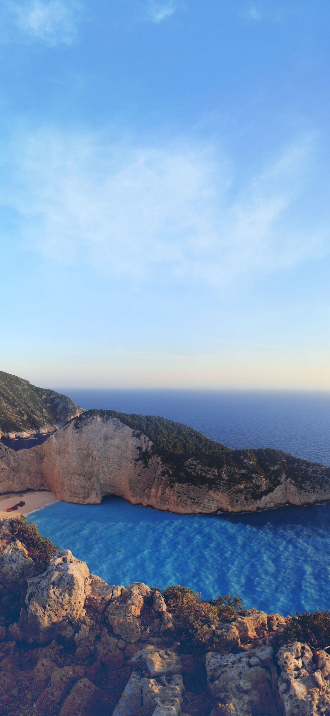 Montaña Rocosa Marrón Junto al Mar Azul Bajo un Cielo Azul Durante el Día. Wallpaper in 1125x2436 Resolution