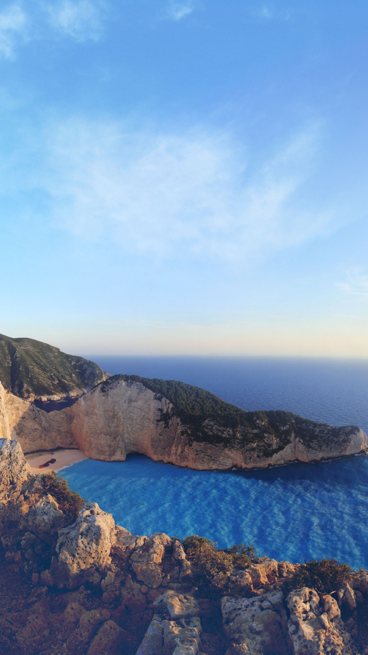 Brown Rocky Mountain Beside Blue Sea Under Blue Sky During Daytime. Wallpaper in 750x1334 Resolution