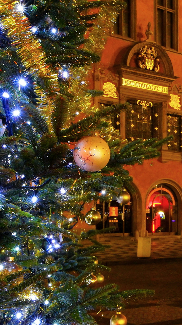 Árbol de Navidad Verde Con Luces de Cadena Cerca Del Edificio de Hormigón Marrón Durante la Noche. Wallpaper in 750x1334 Resolution