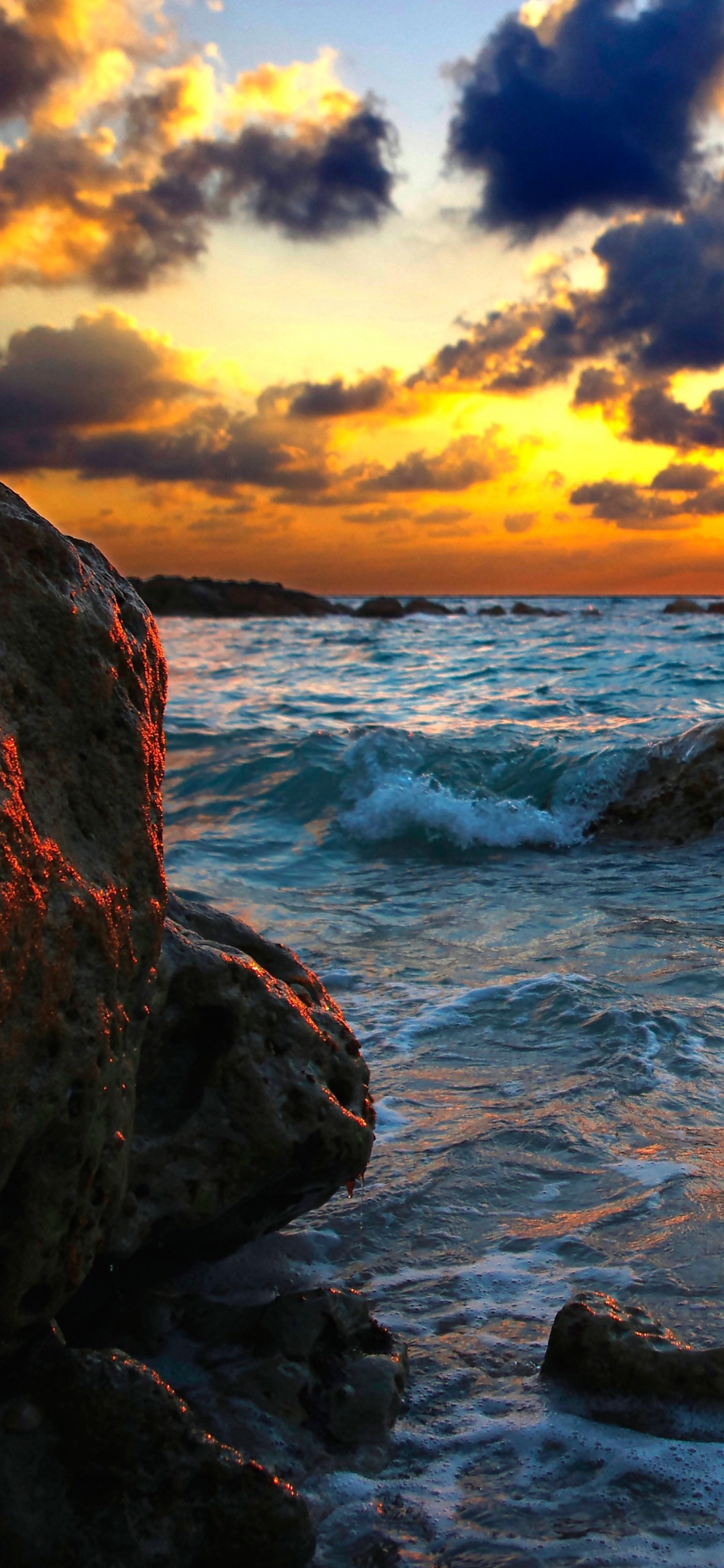 Rocky Shore Under Cloudy Sky During Sunset. Wallpaper in 1125x2436 Resolution