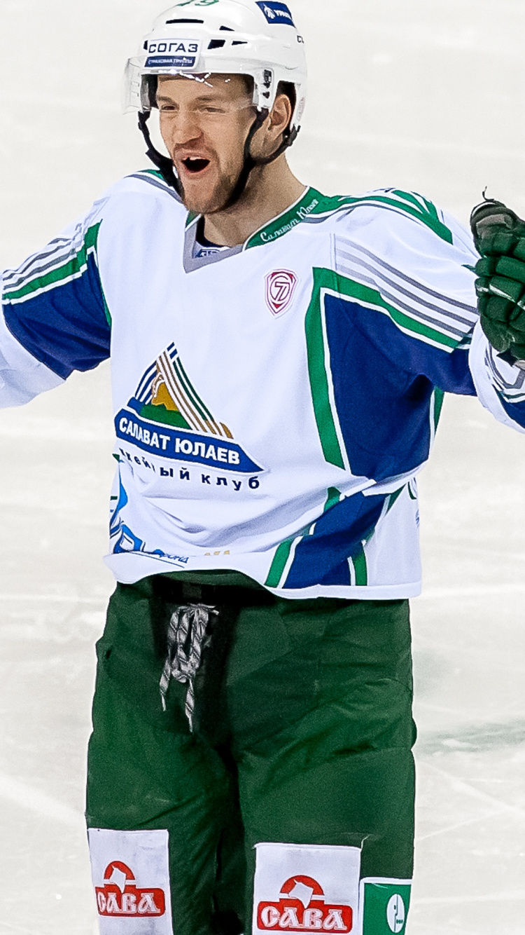 Man in White and Blue Jersey Shirt and Green Pants Holding Black and White Hockey Stick. Wallpaper in 750x1334 Resolution