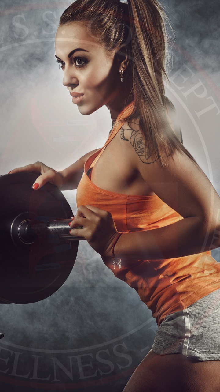 Femme en Débardeur Orange et Short Gris Tenant un Haltère Noir. Wallpaper in 720x1280 Resolution