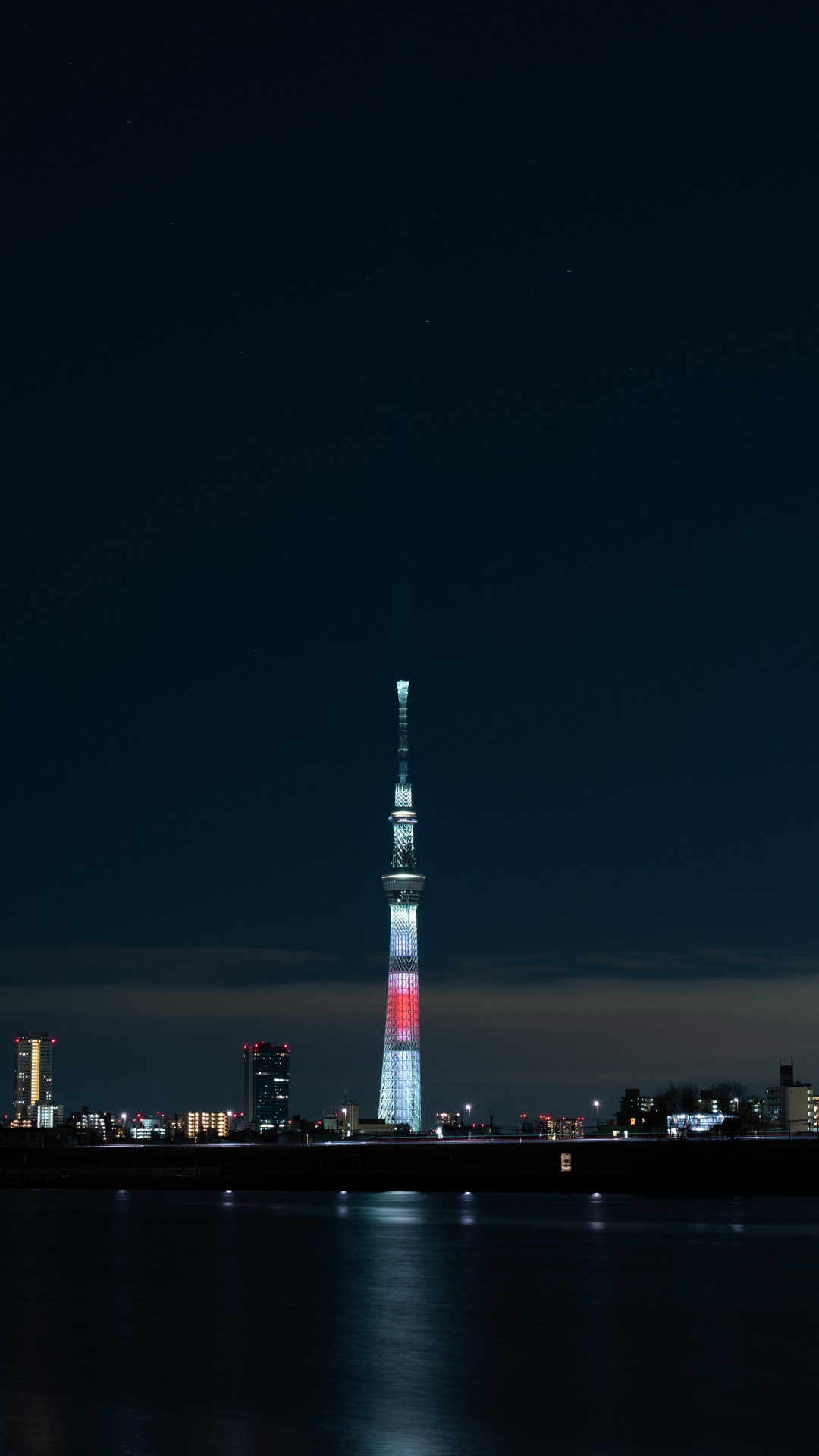 Torre Blanca y Roja Cerca Del Cuerpo de Agua Durante la Noche.. Wallpaper in 1080x1920 Resolution