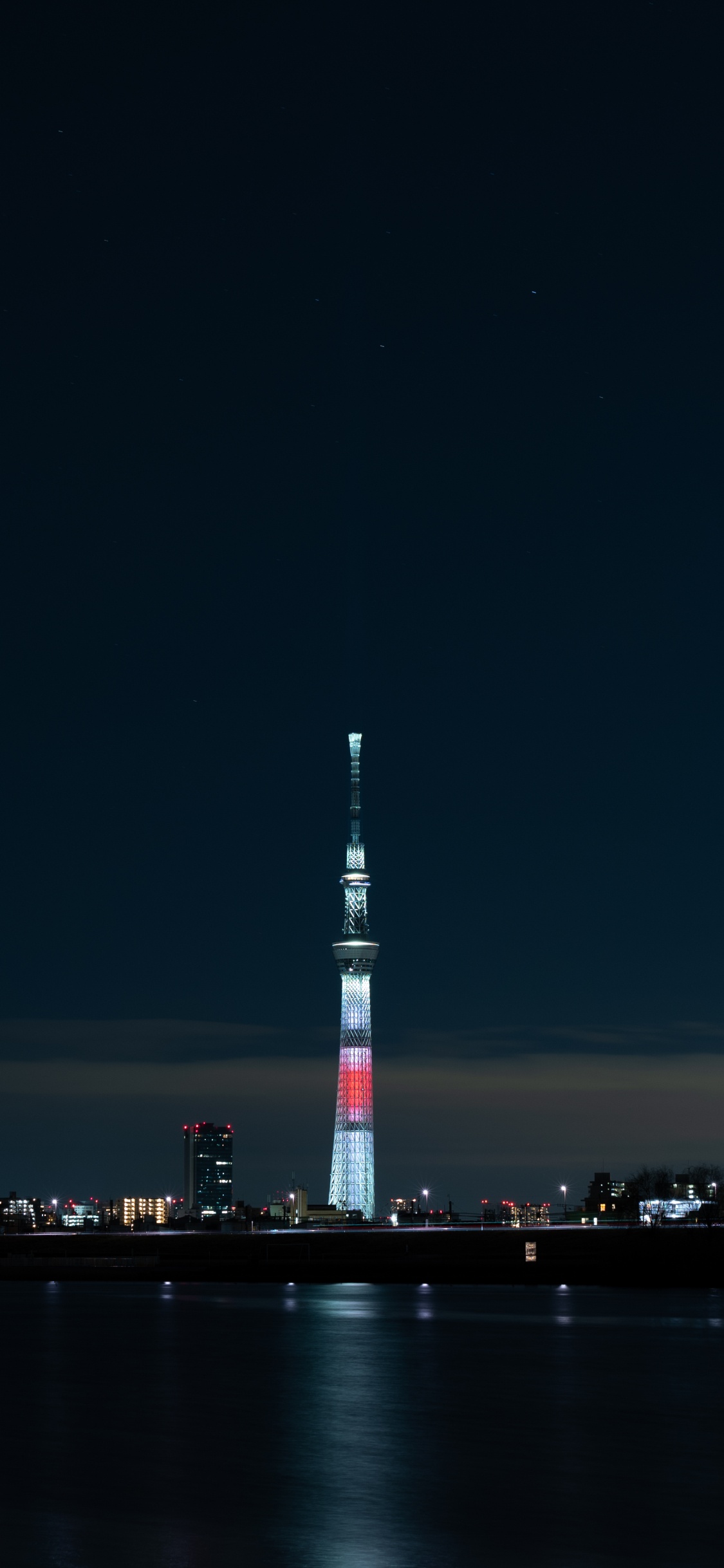 Torre Blanca y Roja Cerca Del Cuerpo de Agua Durante la Noche.. Wallpaper in 1125x2436 Resolution