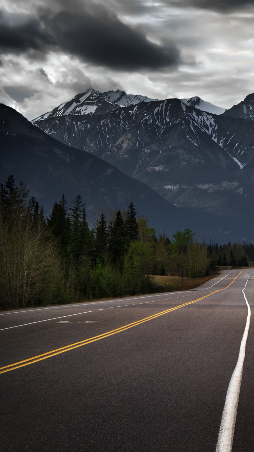 Gray Concrete Road Between Green Trees and Mountain Under Gray Clouds. Wallpaper in 1080x1920 Resolution