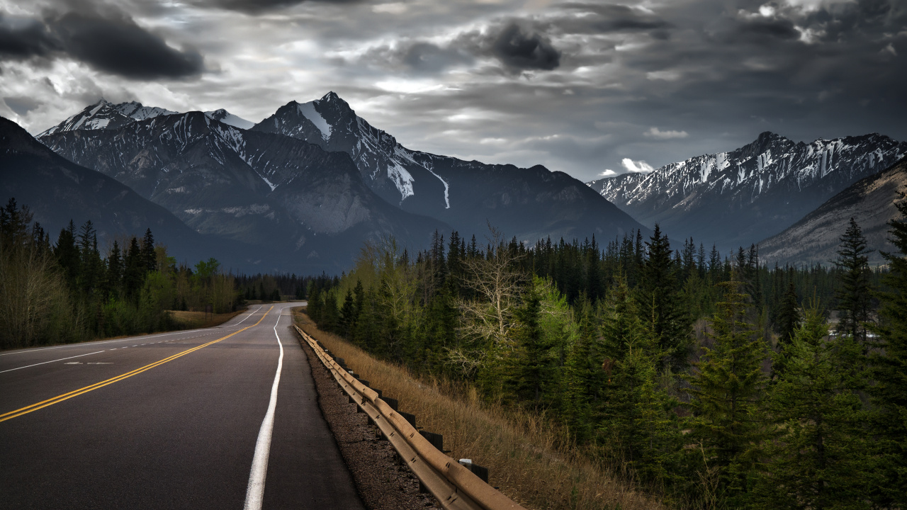 Gray Concrete Road Between Green Trees and Mountain Under Gray Clouds. Wallpaper in 1280x720 Resolution