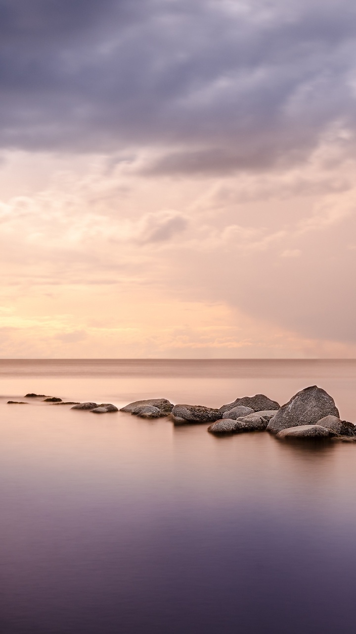 Roches Grises Sur Plan D'eau Sous Des Nuages Gris. Wallpaper in 720x1280 Resolution
