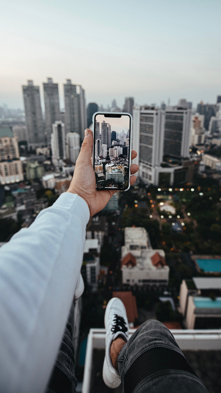Person, Die Ein Schwarzes Smartphone Hält Und Tagsüber Gebäude Der Stadt Fotografiert. Wallpaper in 750x1334 Resolution