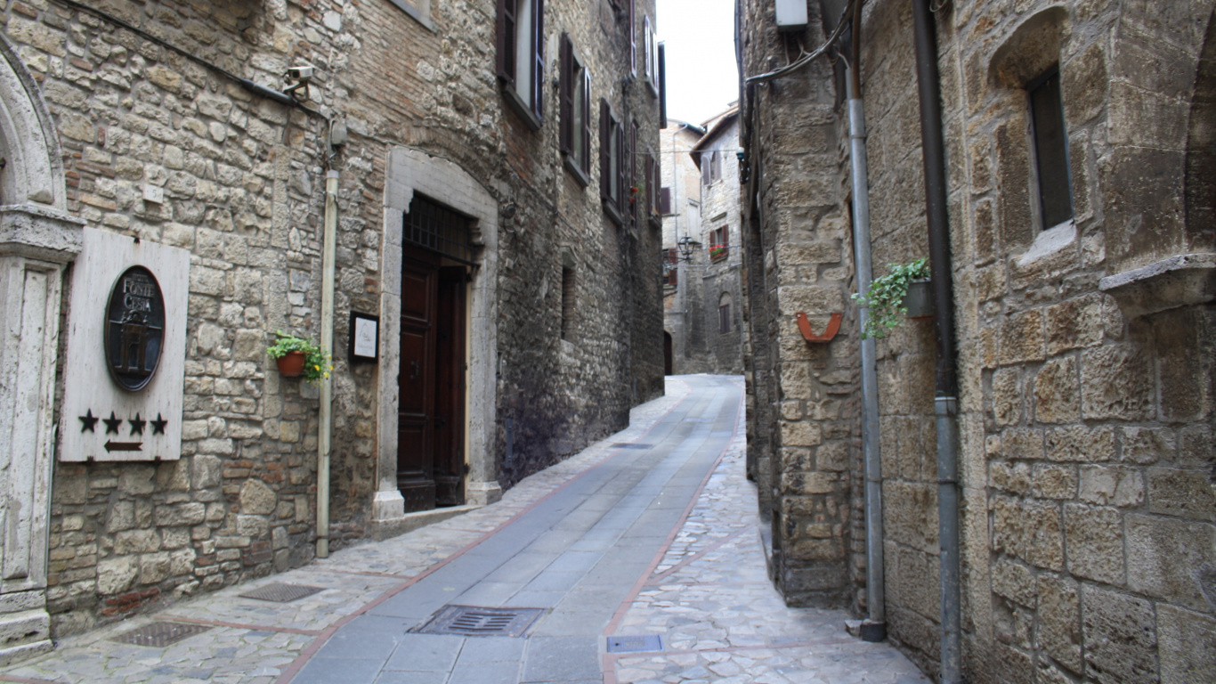 Gray Concrete Pathway Between Brown Brick Buildings During Daytime. Wallpaper in 1366x768 Resolution