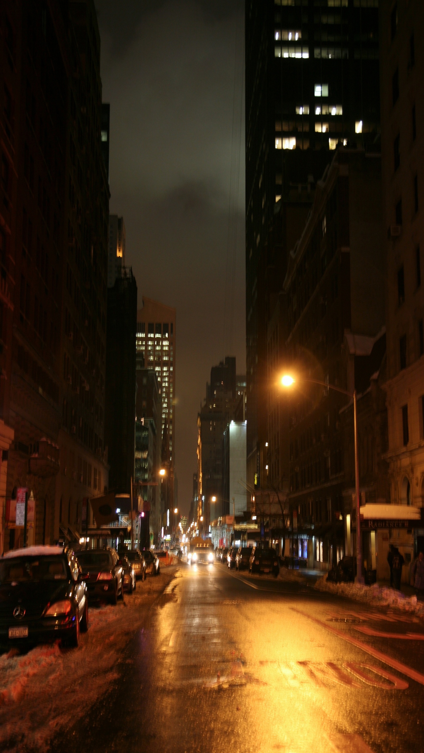 Autos Auf Der Straße Zwischen Hochhäusern Während Der Nacht. Wallpaper in 1440x2560 Resolution