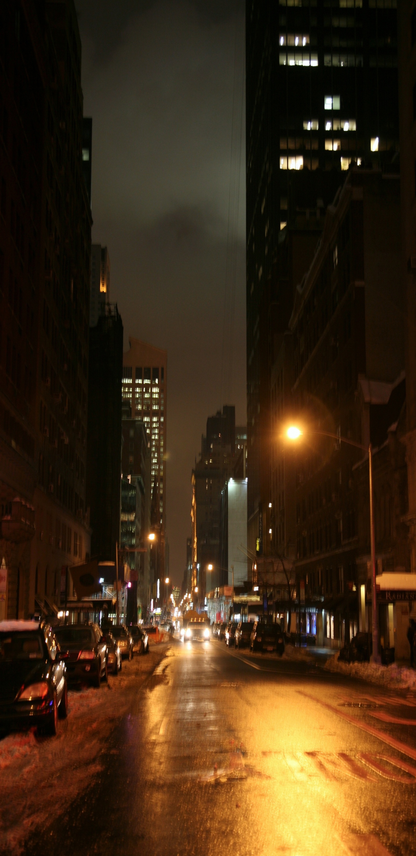 Autos Auf Der Straße Zwischen Hochhäusern Während Der Nacht. Wallpaper in 1440x2960 Resolution