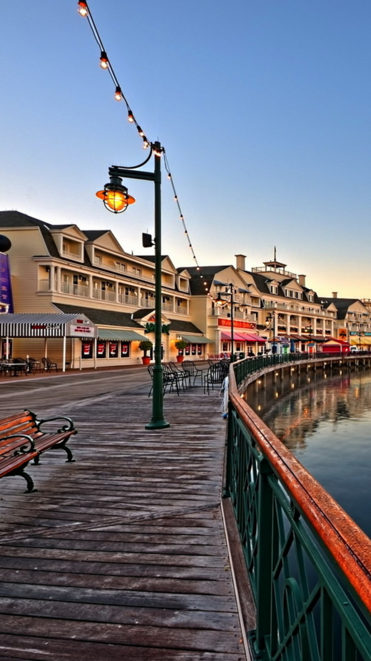 Gente Caminando en la Acera Cerca Del Río Durante la Noche. Wallpaper in 750x1334 Resolution