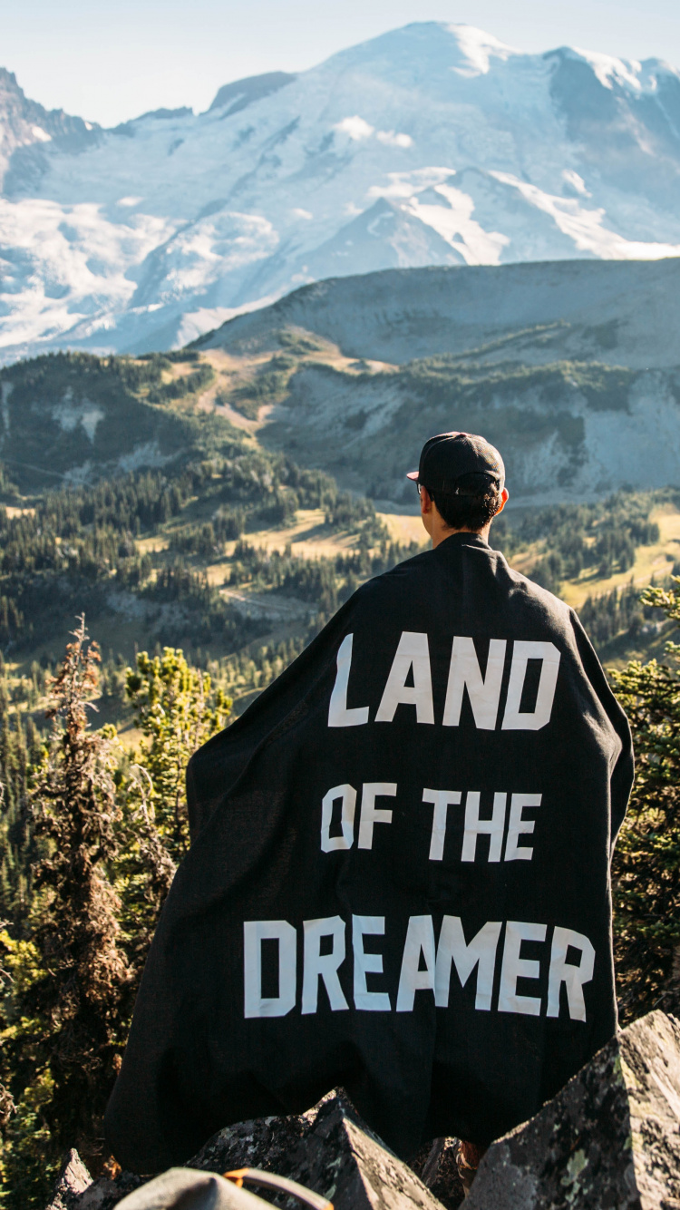Mann in Schwarz-weißer Jacke, Der Auf Grauem Felsen in Der Nähe Grüner Bäume Steht Und Schneebedeckt Ist. Wallpaper in 750x1334 Resolution