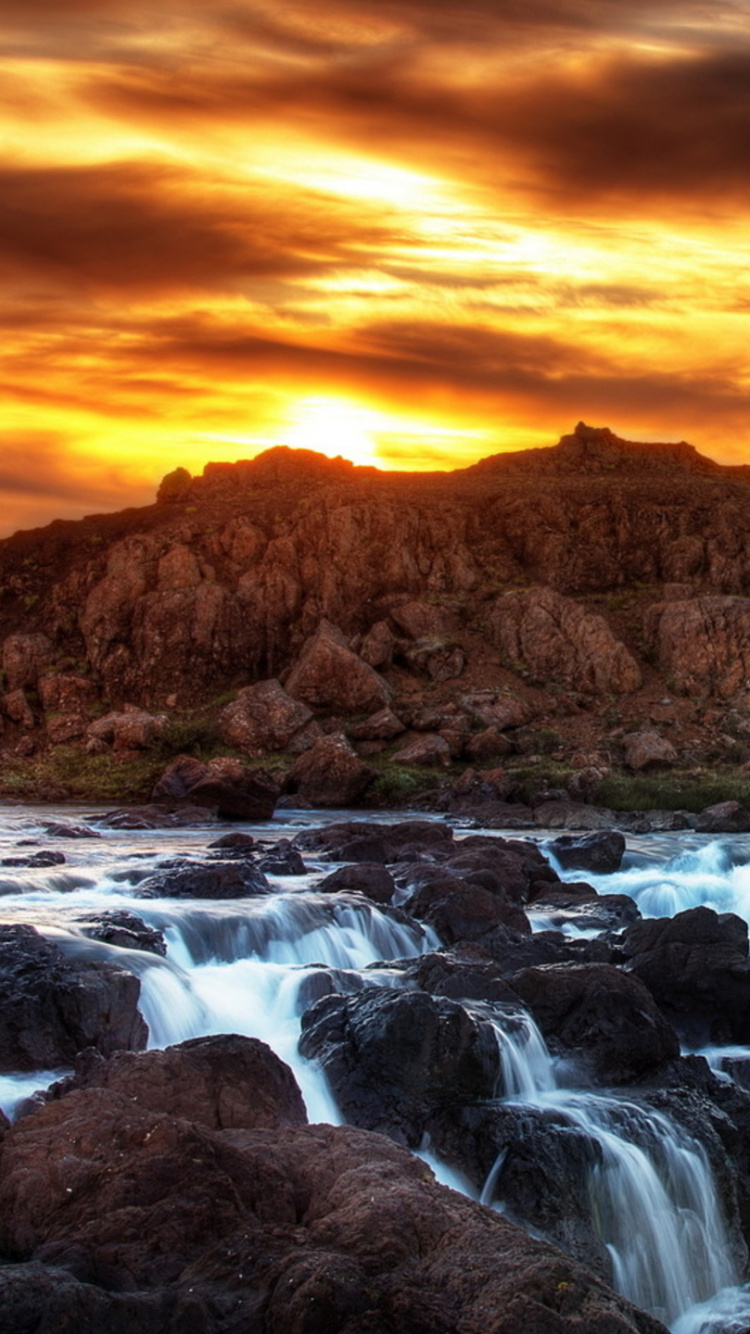 Brauner Felsiger Berg Mit Fluss Bei Sonnenuntergang. Wallpaper in 750x1334 Resolution
