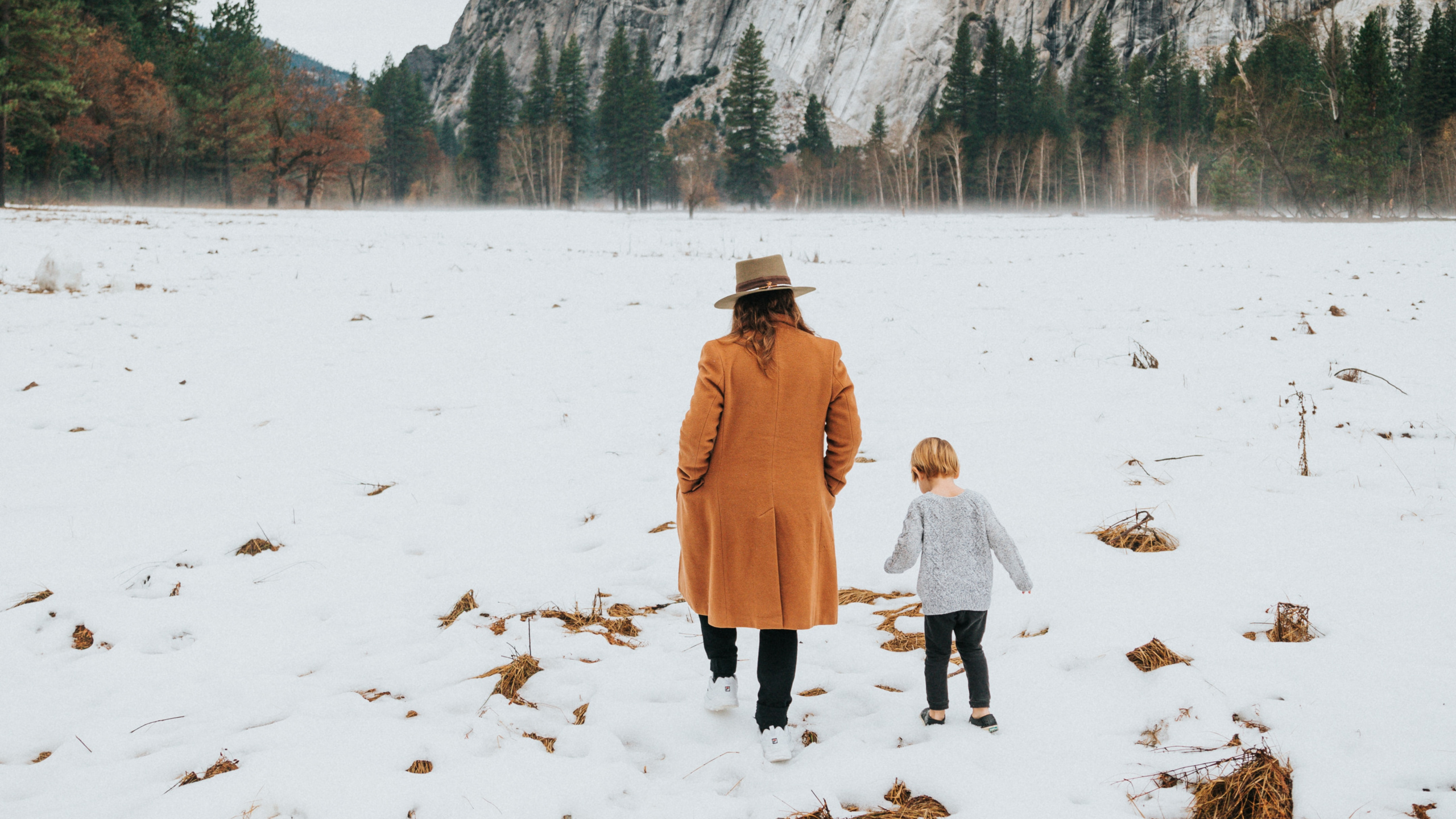 Woman in Brown Coat Walking on Snow Covered Ground During Daytime. Wallpaper in 2560x1440 Resolution