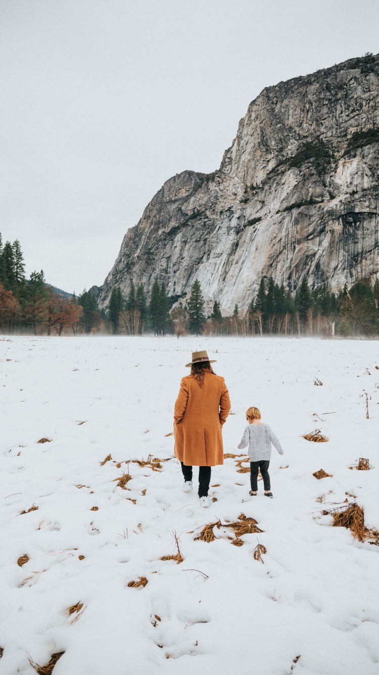 Woman in Brown Coat Walking on Snow Covered Ground During Daytime. Wallpaper in 750x1334 Resolution