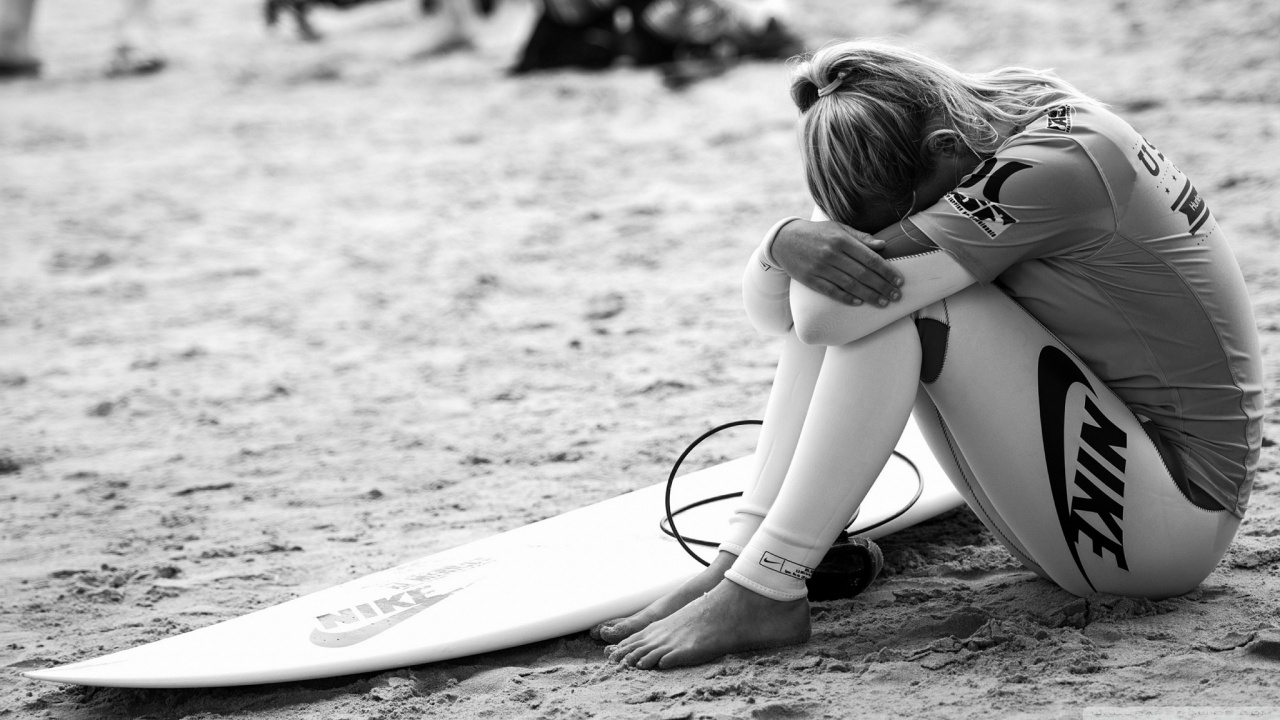 Girl in White Shirt and Black Shorts Sitting on White Surfboard on Beach During Daytime. Wallpaper in 1280x720 Resolution