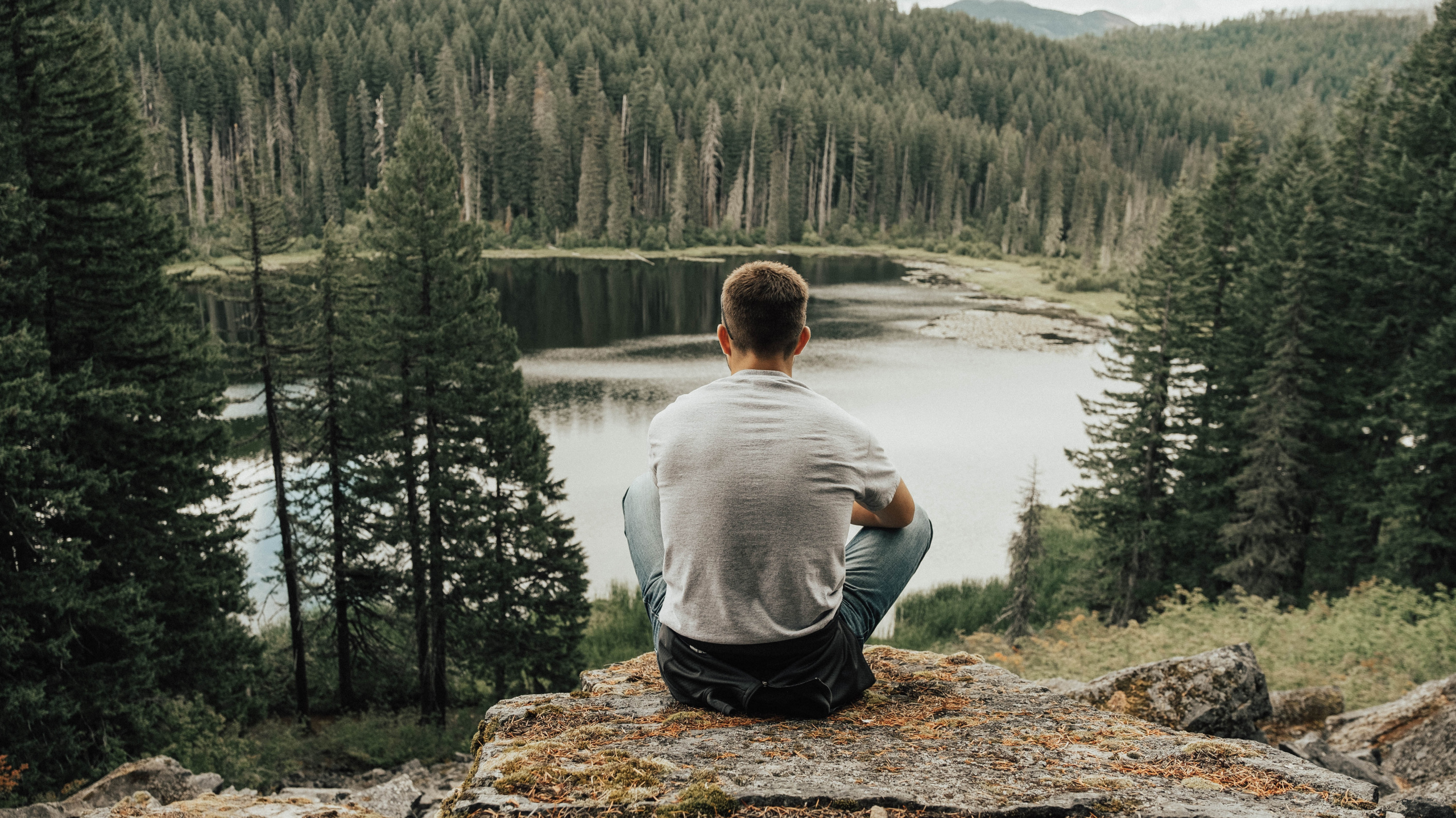 Man in Gray Sweater Sitting on Brown Rock Near Lake During Daytime. Wallpaper in 2560x1440 Resolution