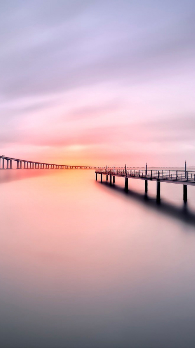 Bridge Over Body of Water Under Cloudy Sky. Wallpaper in 750x1334 Resolution