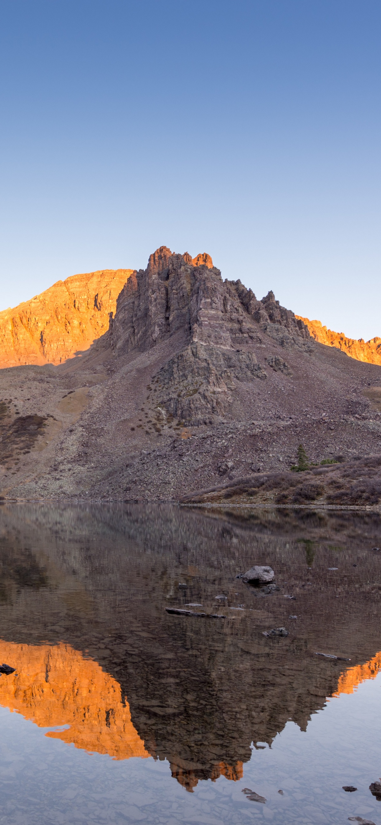 Brown Rocky Mountain Beside Body of Water During Daytime. Wallpaper in 1242x2688 Resolution