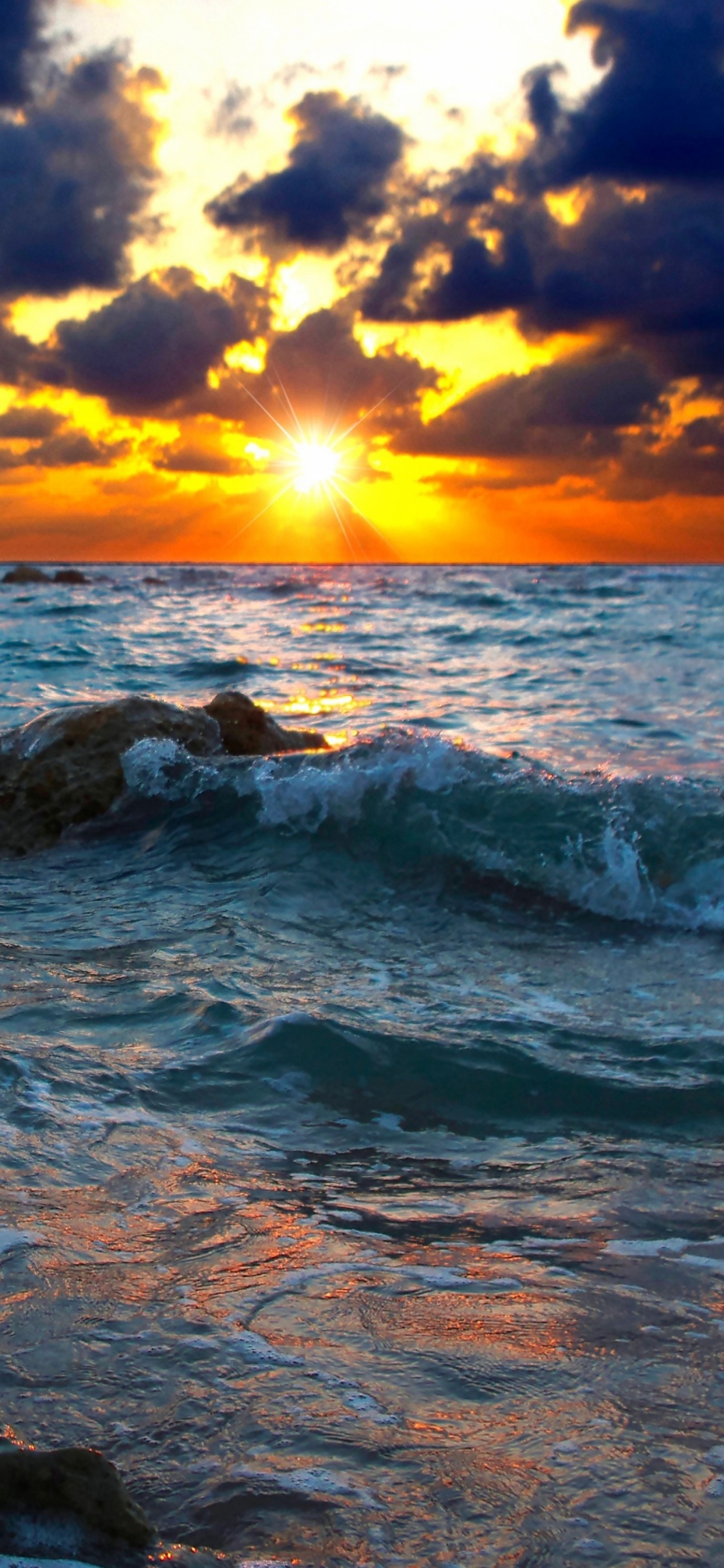 Rocky Shore Under Cloudy Sky During Sunset. Wallpaper in 1125x2436 Resolution