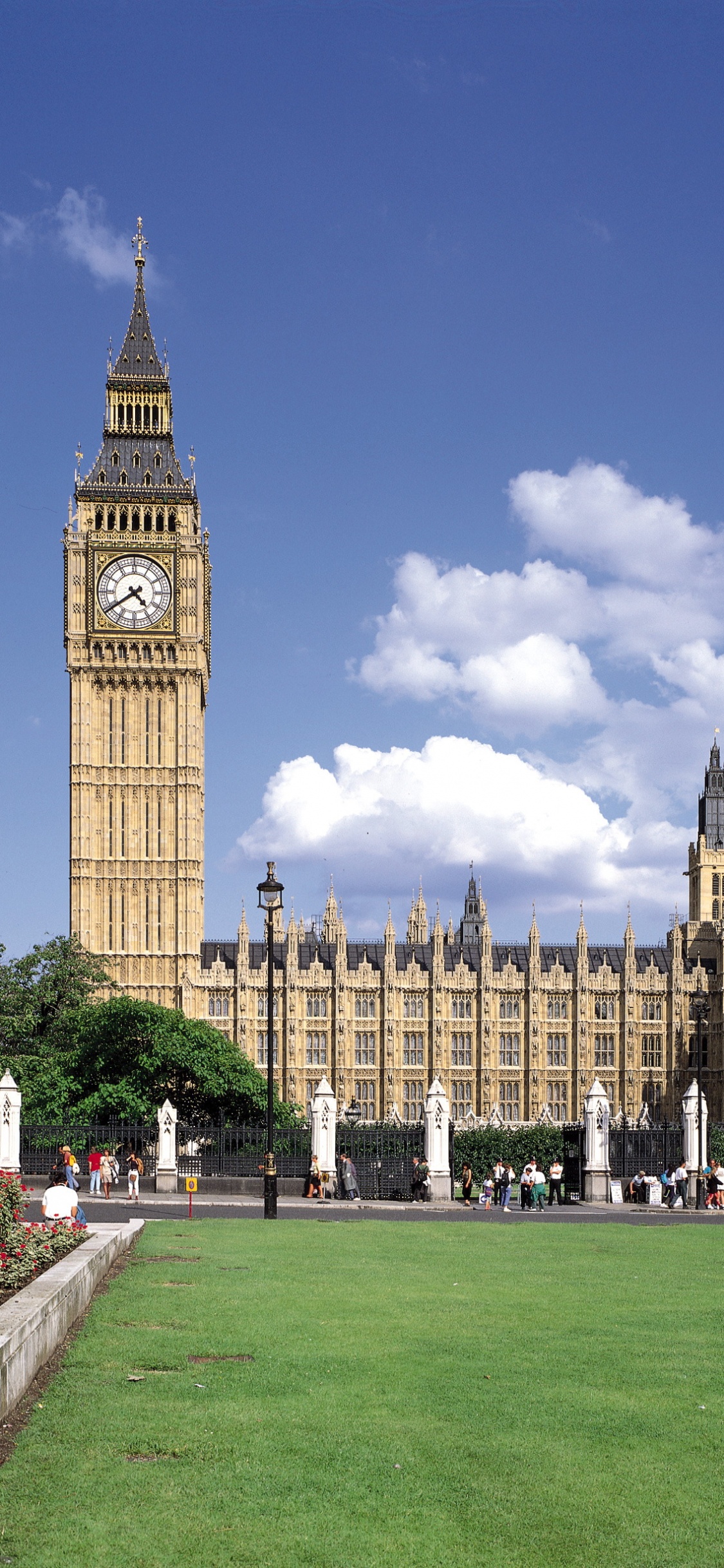 People Walking on Green Grass Field Near Brown Concrete Building During Daytime. Wallpaper in 1125x2436 Resolution