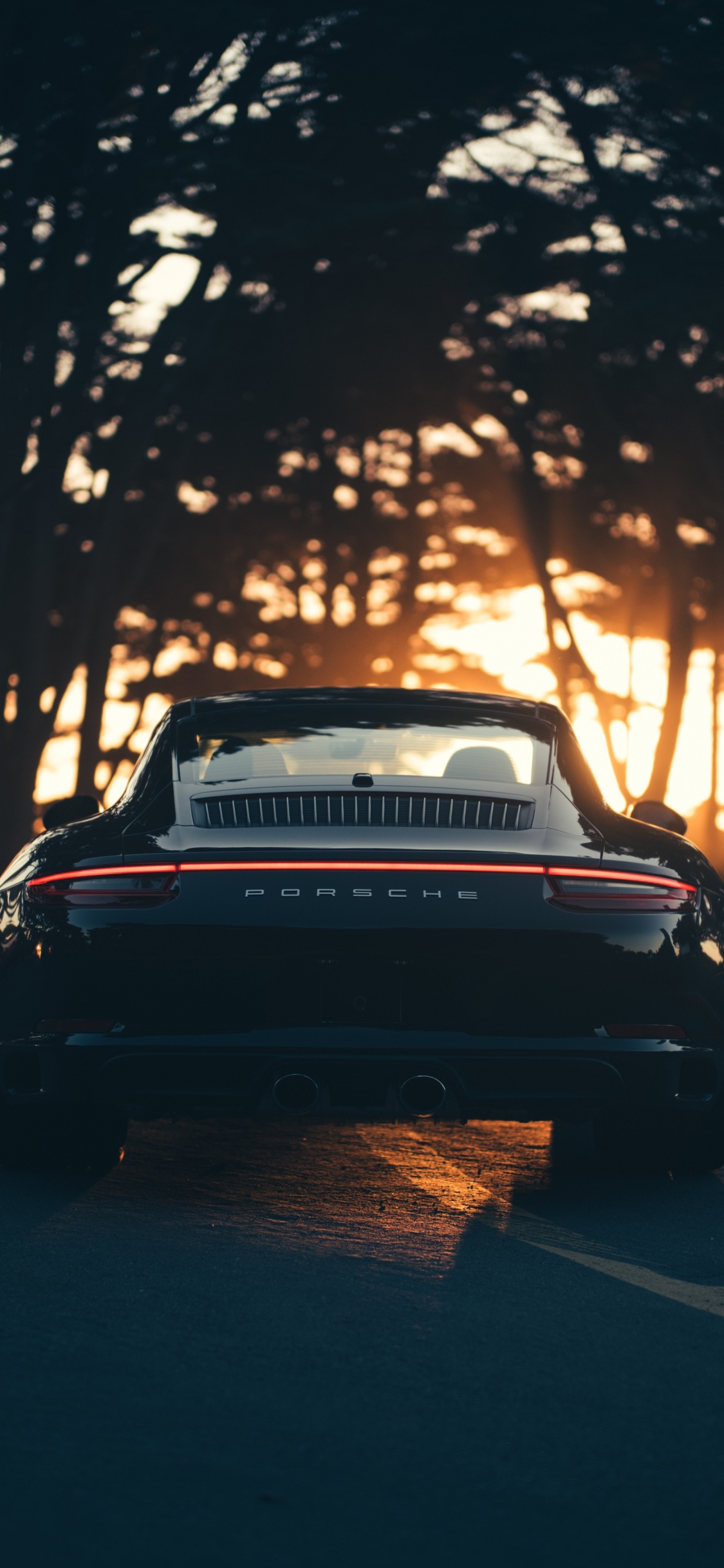 Schwarzes Auto Auf Der Straße Bei Sonnenuntergang. Wallpaper in 1125x2436 Resolution