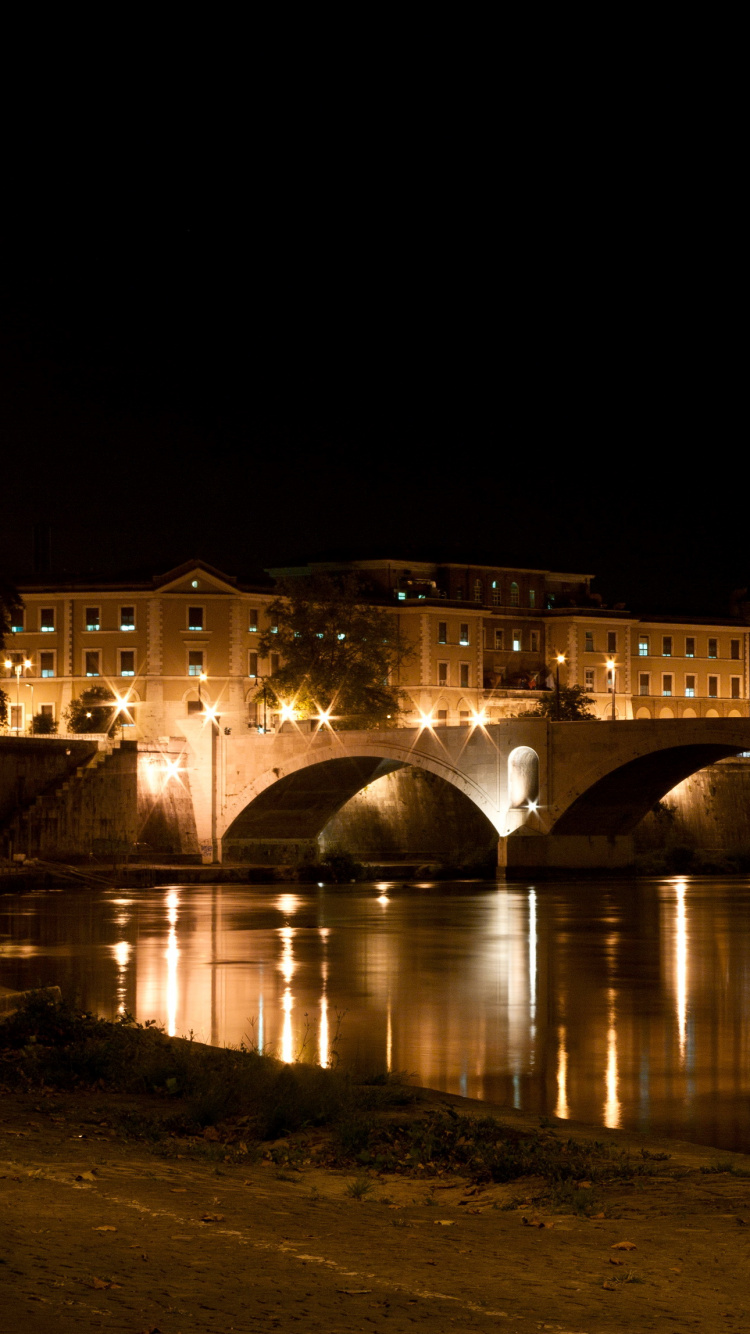 Edificio de Hormigón Marrón Cerca Del Cuerpo de Agua Durante la Noche. Wallpaper in 750x1334 Resolution