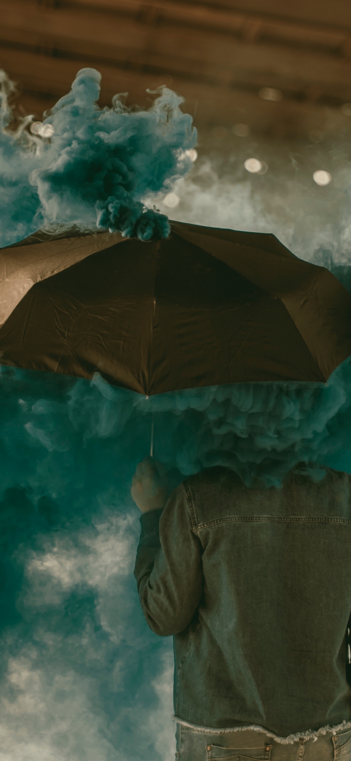 Person in Brown Jacket Holding Umbrella Under White Clouds. Wallpaper in 1125x2436 Resolution