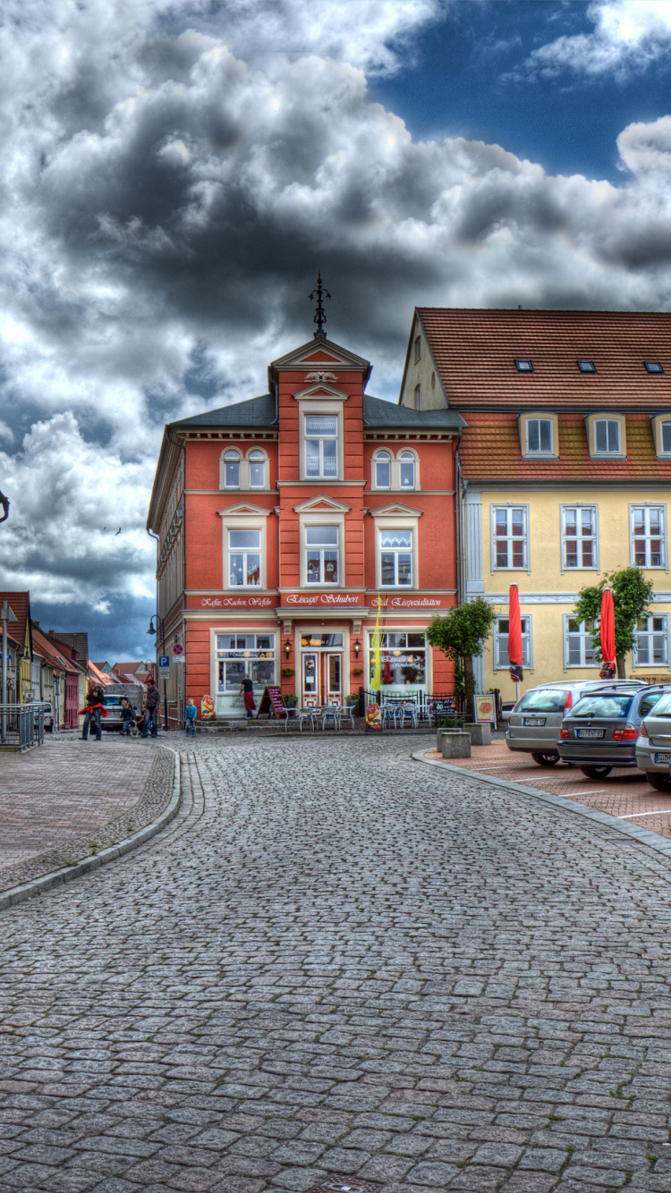 Los Coches Aparcados Junto al Edificio de Hormigón Marrón Bajo un Cielo Nublado Durante el Día. Wallpaper in 750x1334 Resolution