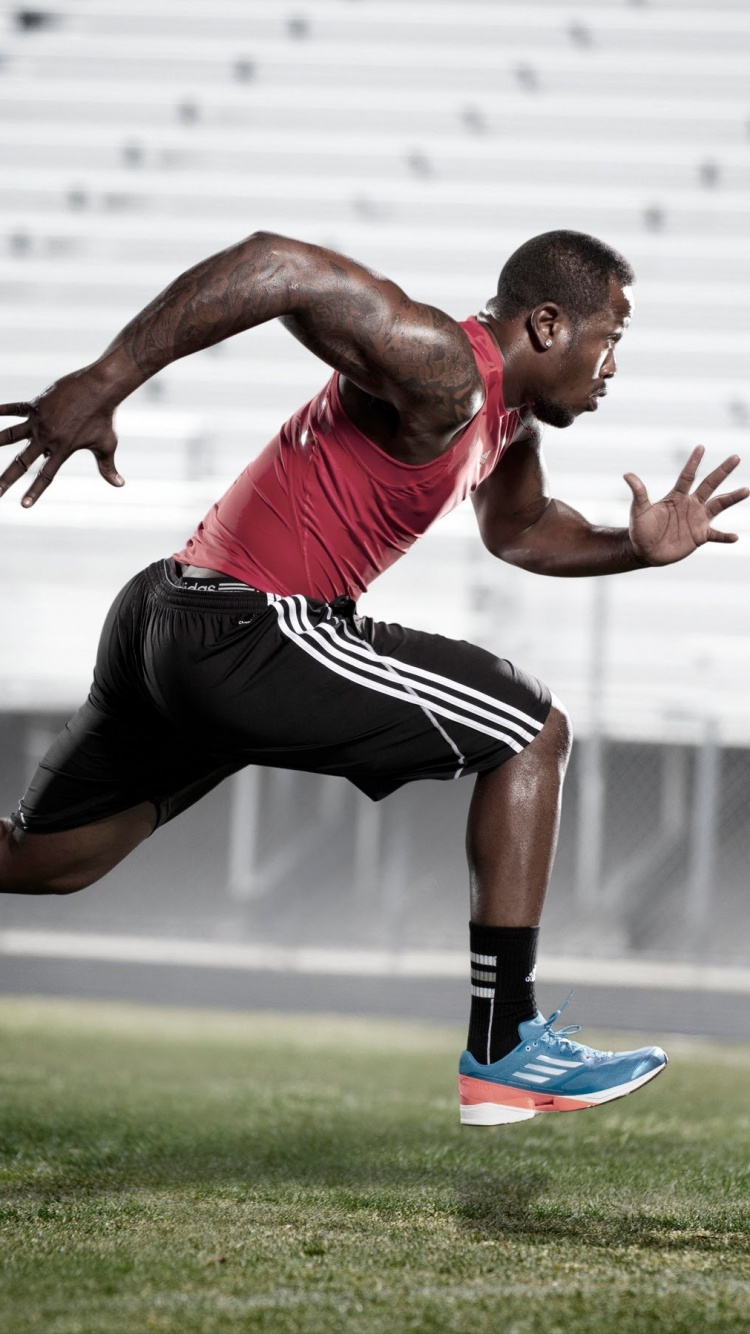 Man in Red Tank Top and Black Shorts Running on Green Grass Field During Daytime. Wallpaper in 750x1334 Resolution