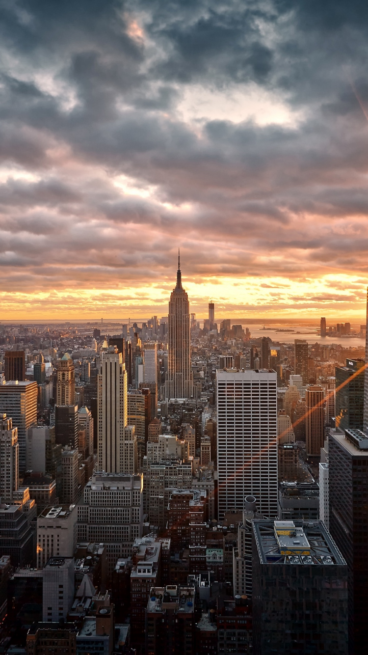 Skyline Der Stadt Unter Orange Und Grau Bewölktem Himmel Bei Sonnenuntergang. Wallpaper in 750x1334 Resolution