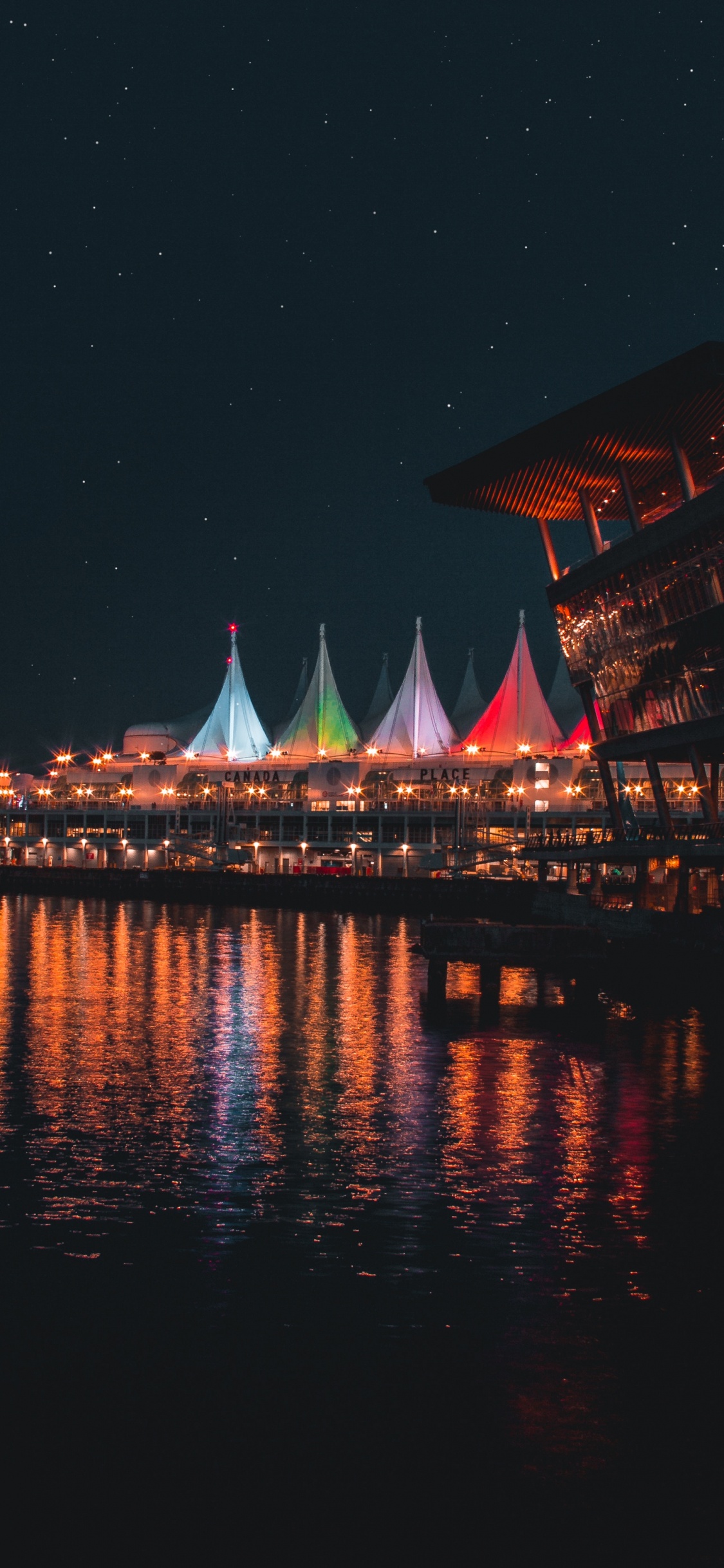 Edificio Marrón y Blanco Cerca Del Cuerpo de Agua Durante la Noche.. Wallpaper in 1125x2436 Resolution